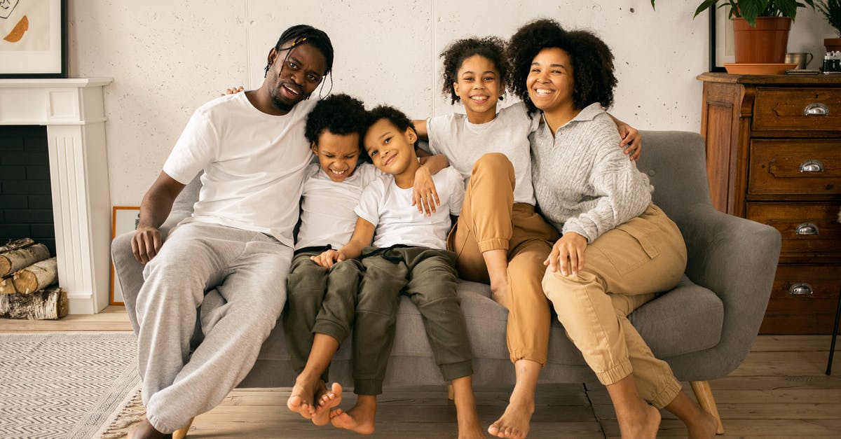 I live in the US. My sister just passed in Canada - Full body of cheerful African American parents with children looking at camera while sitting on sofa in room with fireplace I live in the US. My sister just passed in Canada - Full body of cheerful African American parents with children looking at camera while sitting on sofa in room with fireplace