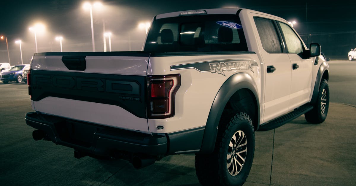 Ibiza car hire late at night - White pickup truck on parking lot with cars under shiny streetlamps at night Ibiza car hire late at night - White pickup truck on parking lot with cars under shiny streetlamps at night