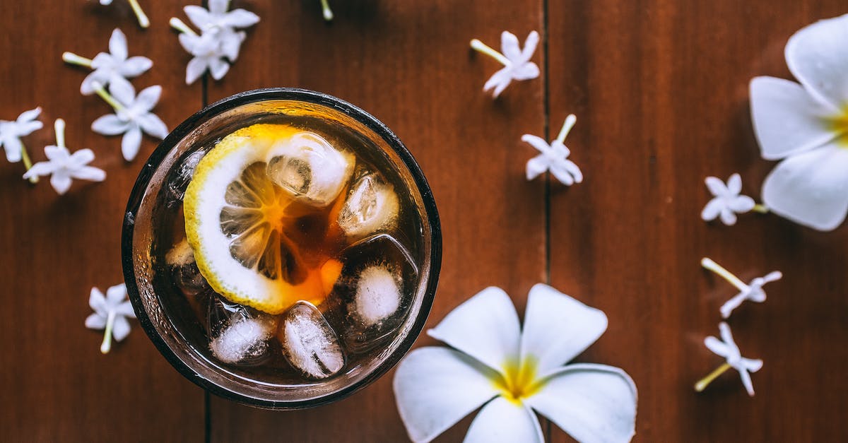 ICE from Frankfurt to Limburg - Top view of glass with fresh drink with slice of lemon and ice cubes on wooden background with plumeria flowers ICE from Frankfurt to Limburg - Top view of glass with fresh drink with slice of lemon and ice cubes on wooden background with plumeria flowers
