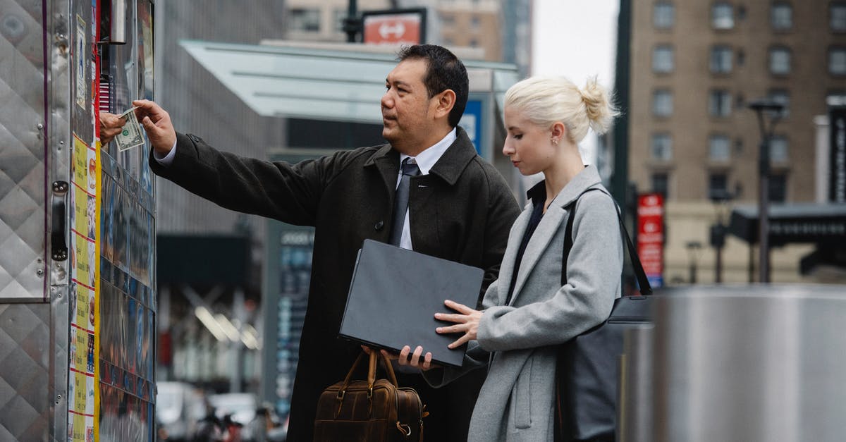 If I buy a 1-day Travelcard (Zone 1-9), can I use it to go from London downtown to Gatwick? - Side view of middle aged ethnic businessman paying for purchases while standing with young female colleague on street during break