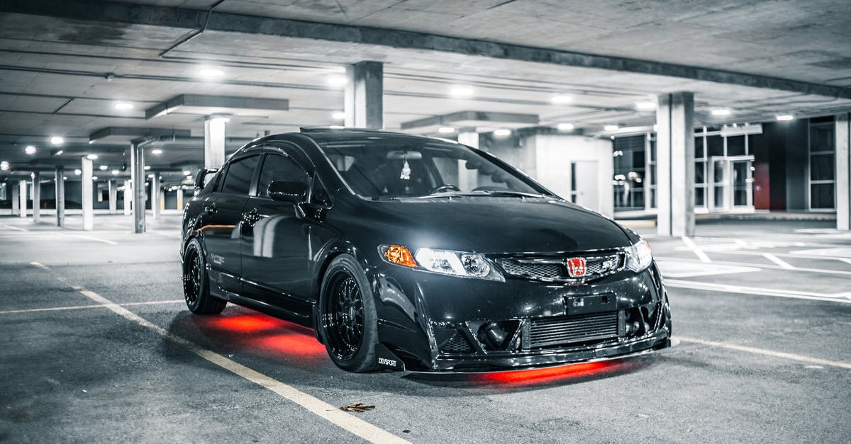 In Italy, how to know parking fee before driving into the parking lot? - Modern black automobile with glowing headlights and illumination in underground parking lot with marking lines and columns in evening time