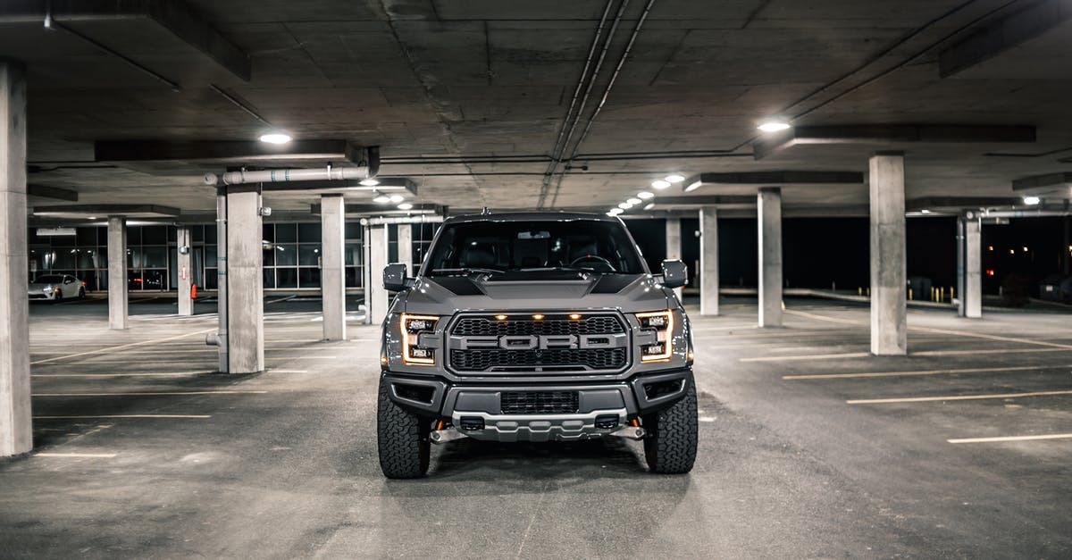 In Italy, how to know parking fee before driving into the parking lot? - Modern gray pickup with glowing headlights parked on asphalt in underground parking lot with columns in evening time in city