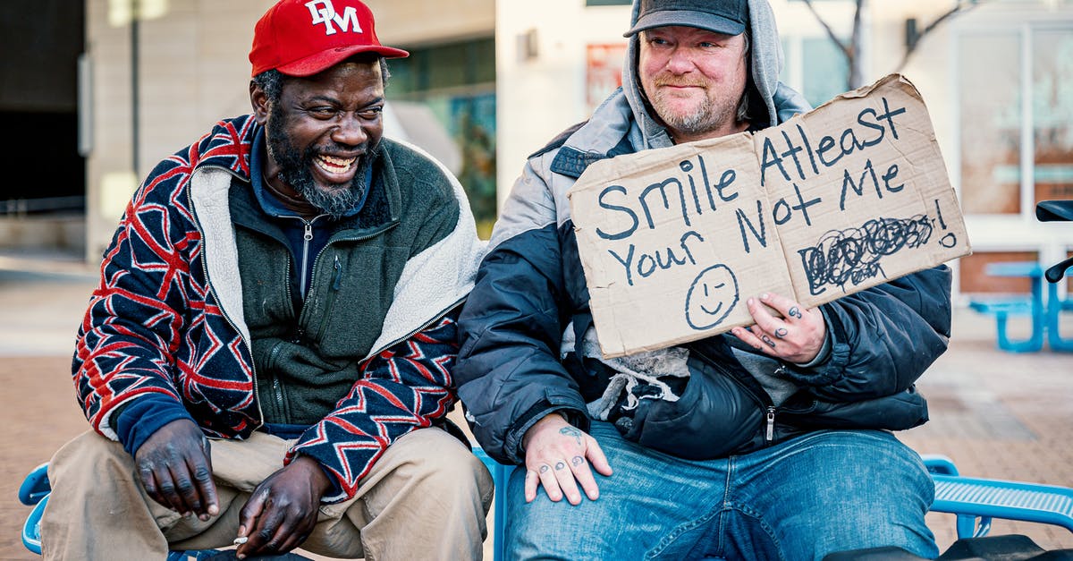 In Schengen visa application, should I include details of my friend who will be spending time with me? - Positive middle aged man showing carton with smile at least your not me inscription while sitting on bench with laughing African American male friend