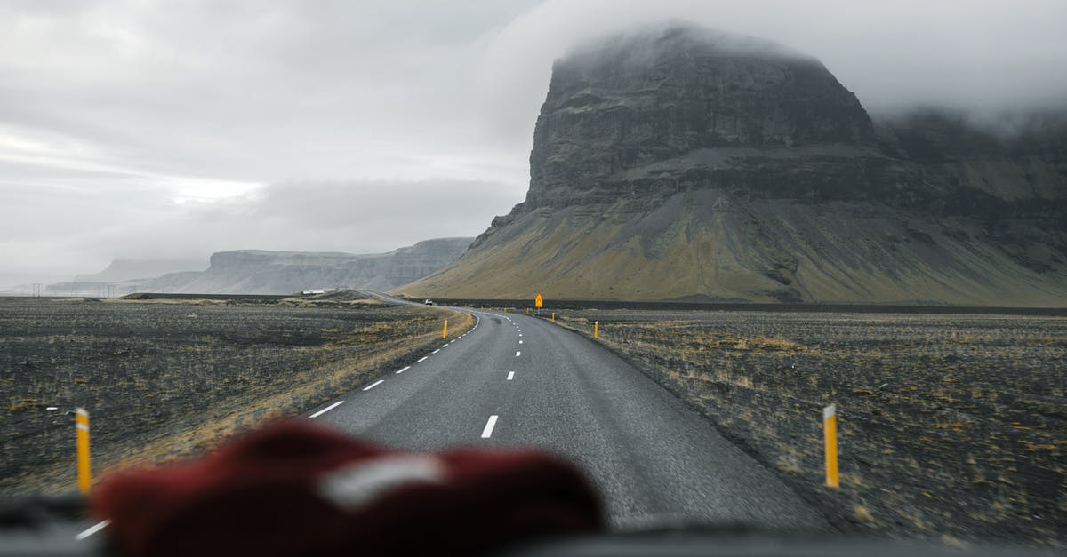 In the US, should I rent a car through travel agencies or directly with car rental companies? - Through glass of empty asphalt road going through valley with mountain slopes against foggy sky