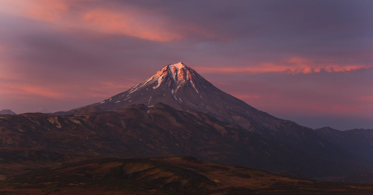Inclement weather at destination airport during layover in a foreign country - Terrain with rocky surface against mountain ranges with snowy peak under cloudy sky at sundown