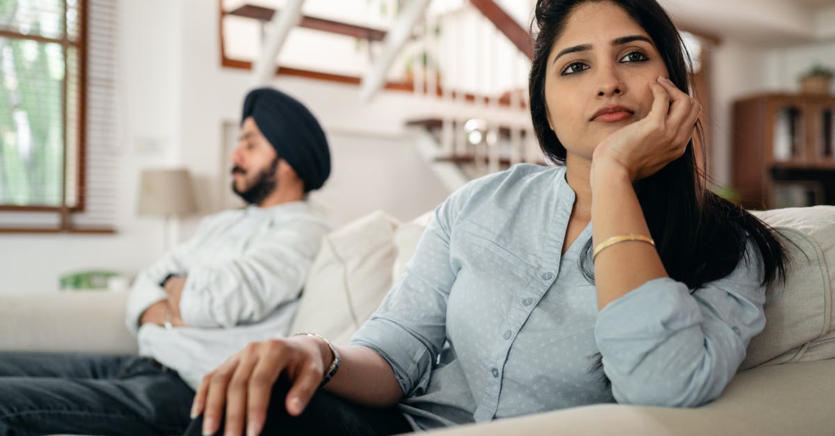 Indian eBusiness visa issues - Sad young Indian woman avoiding talking to husband while sitting on sofa Indian eBusiness visa issues - Sad young Indian woman avoiding talking to husband while sitting on sofa