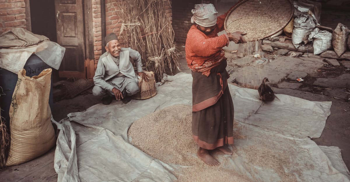 Indian eVisa Process - Anonymous barefoot Hindu female pouring rice from sieve on textile near content senior male in daytime Indian eVisa Process - Anonymous barefoot Hindu female pouring rice from sieve on textile near content senior male in daytime
