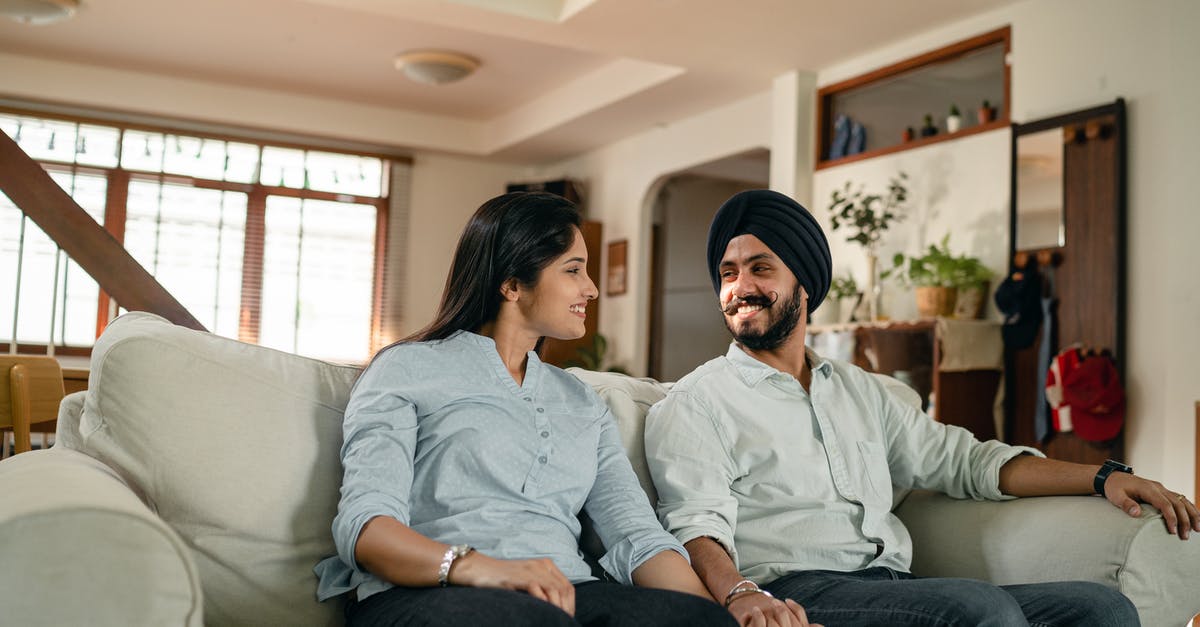 Indian National, Living in New Zealand looking to go to Europe [closed] - Happy smiling young Indian couple in similar outfits holding hands and looking at each other while resting on sofa in cozy living room