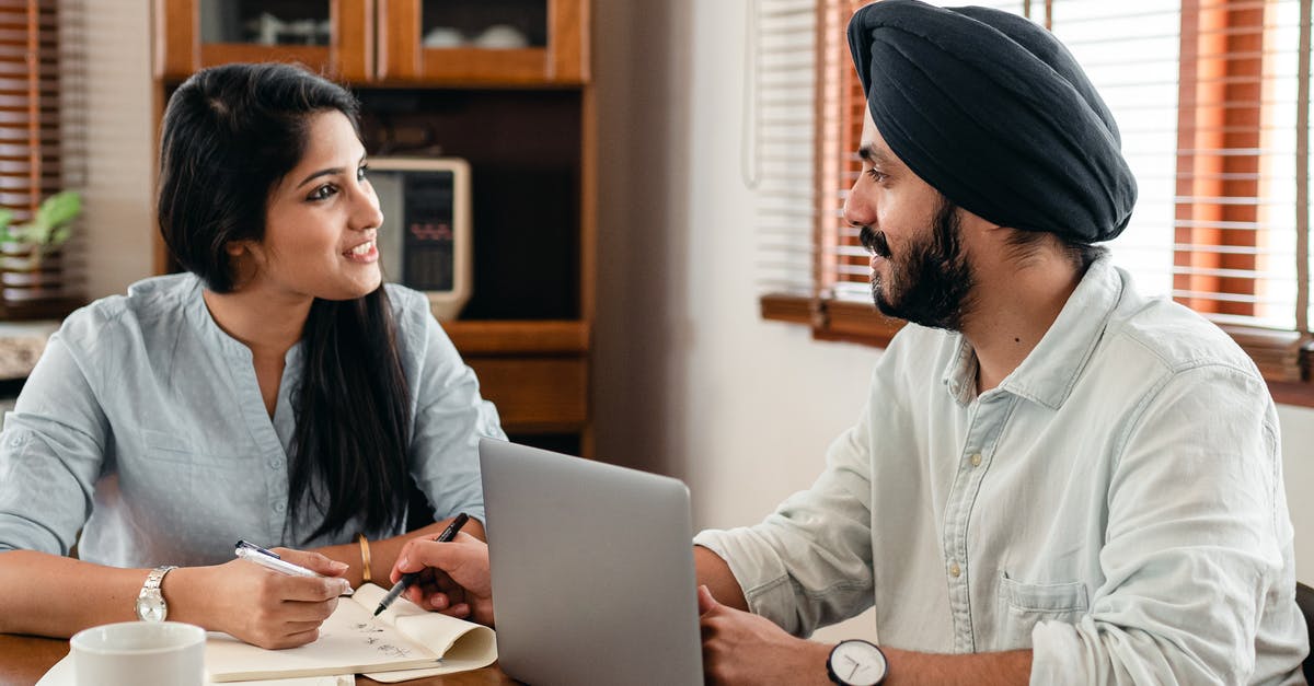 Indian Railways-Online Reservation Rules - Indian male in turban and wristwatch typing on netbook while interacting with happy female coworker with notebook and pen sitting at table in office and looking at each other Indian Railways-Online Reservation Rules - Indian male in turban and wristwatch typing on netbook while interacting with happy female coworker with notebook and pen sitting at table in office and looking at each other
