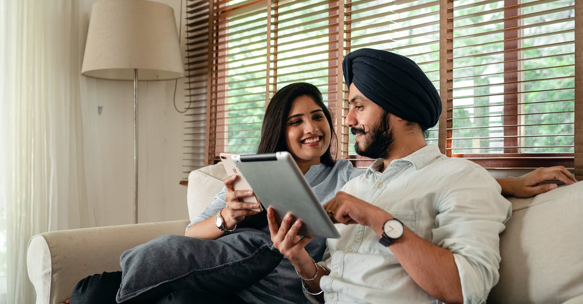 Indian Railways-Online Reservation Rules - Calm ethnic couple browsing tablet and sitting in living room Indian Railways-Online Reservation Rules - Calm ethnic couple browsing tablet and sitting in living room