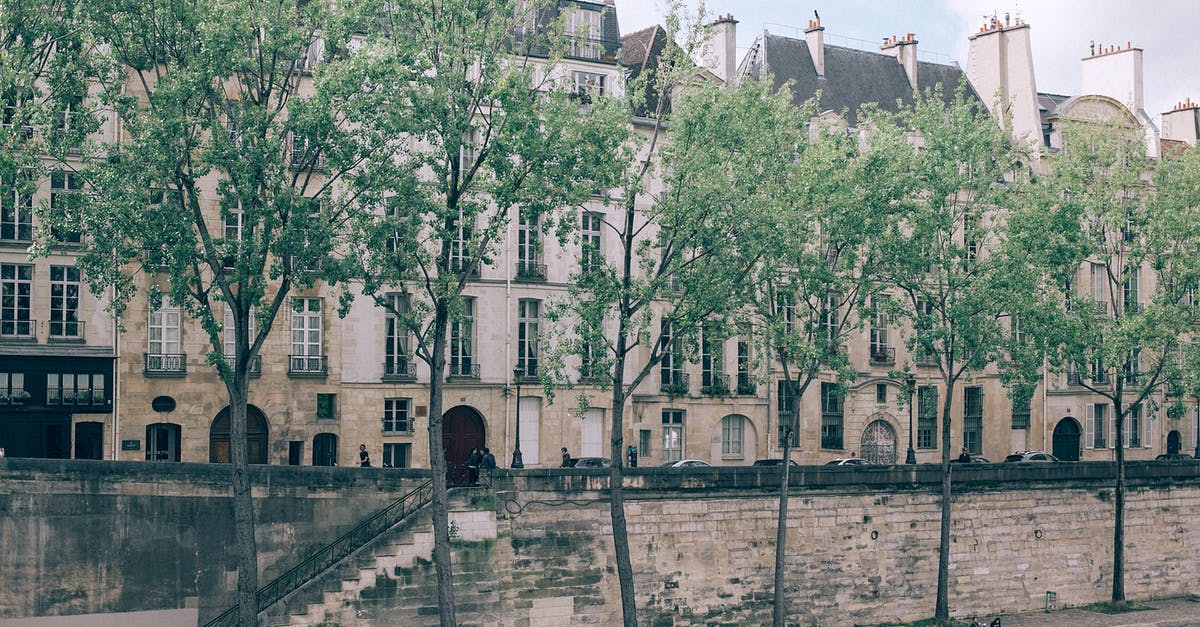 Indian traveling to Thailand with residence in Europe - Narrow walkway with green trees between river and city street with old high buildings Indian traveling to Thailand with residence in Europe - Narrow walkway with green trees between river and city street with old high buildings
