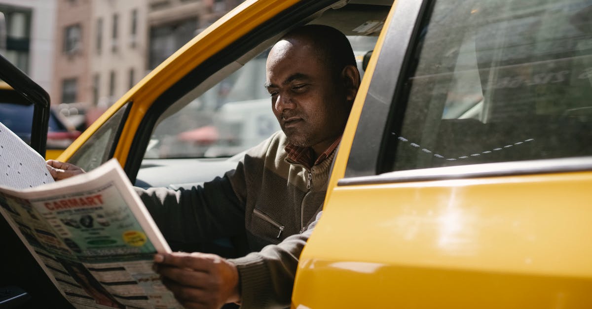 Information about public transport in Greece - Concentrated male driver in casual clothes sitting in taxi during break and reading newspaper Information about public transport in Greece - Concentrated male driver in casual clothes sitting in taxi during break and reading newspaper