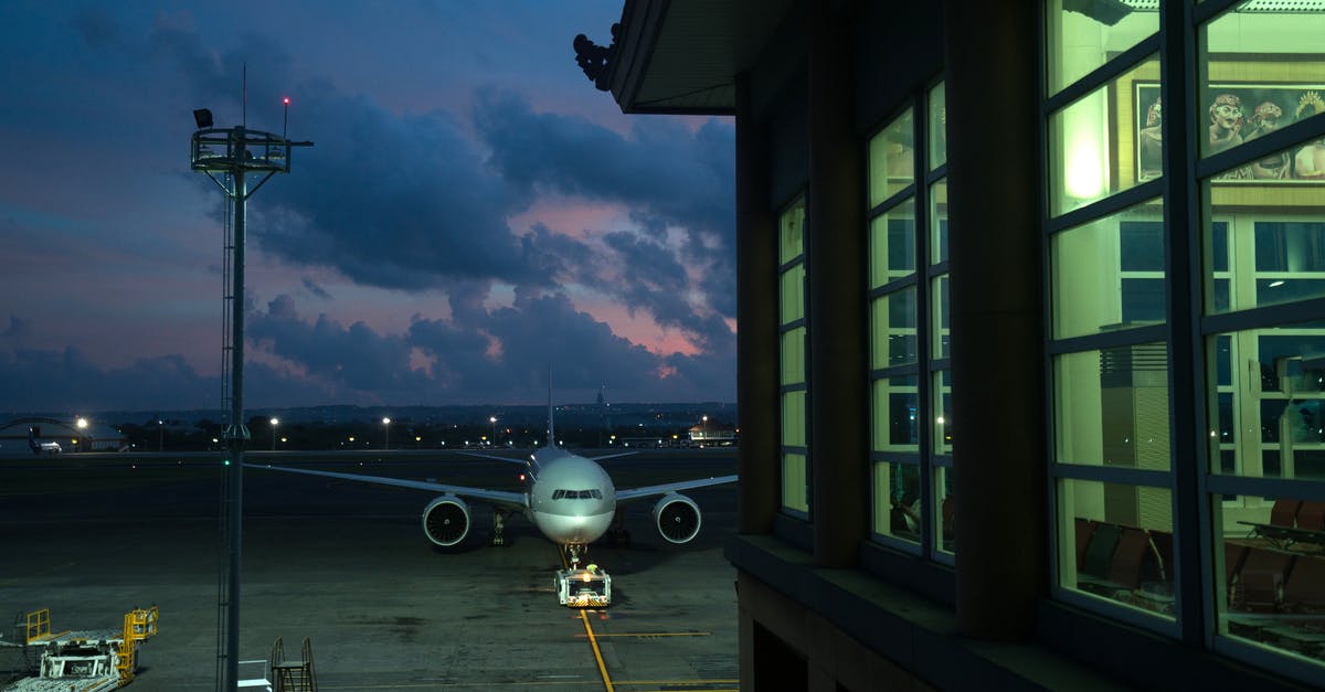 International travel with connecting flights with different airlines - Modern plane parking on stand near assigned gate in modern airport terminal at night