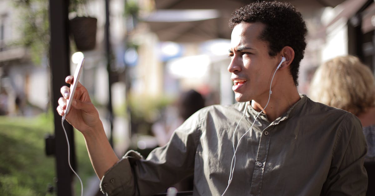Internet access using mobile phone in Argentina - Side view of black male wearing summer shirt using smartphone for video chatting and sitting on outdoor terrace while communicating on social media Internet access using mobile phone in Argentina - Side view of black male wearing summer shirt using smartphone for video chatting and sitting on outdoor terrace while communicating on social media