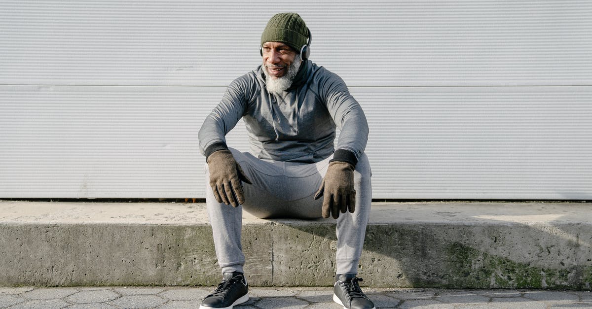 Is appearance important at the border? - Full body of positive African American male wearing trendy outfit listening to music with headphones while sitting on concrete border of road Is appearance important at the border? - Full body of positive African American male wearing trendy outfit listening to music with headphones while sitting on concrete border of road