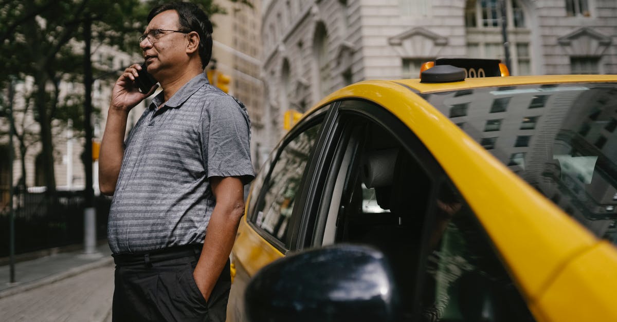 Is it acceptable to request a taxi driver stop using their phone while driving? - Serious ethnic male taxi driver with hand in pocket having conversation on cellphone while standing near car Is it acceptable to request a taxi driver stop using their phone while driving? - Serious ethnic male taxi driver with hand in pocket having conversation on cellphone while standing near car