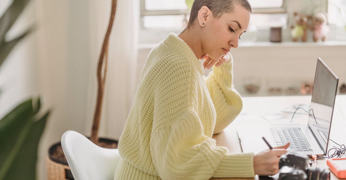 Is it allowed to take an external hard drive with you on a plane? - Side view of serious female with short hair drawing with stylus while editing photos at table with photo camera during work in room with green plant