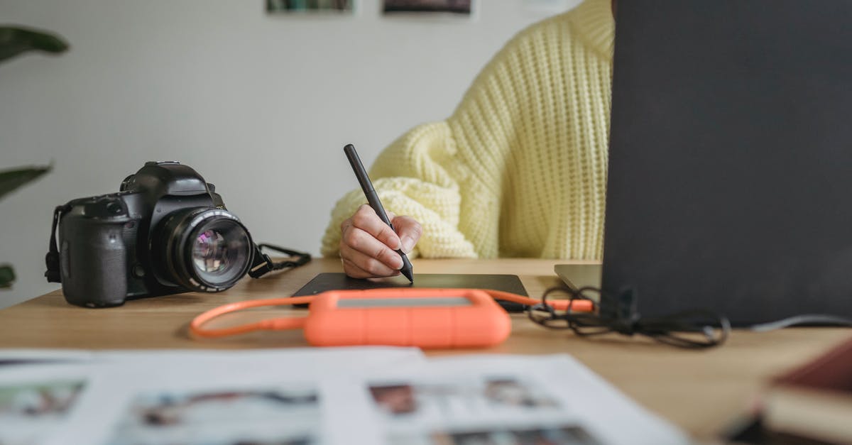 Is it allowed to take an external hard drive with you on a plane? - Crop anonymous woman using graphic tablet while editing photos on netbook at table with photo camera and blurred printed photos