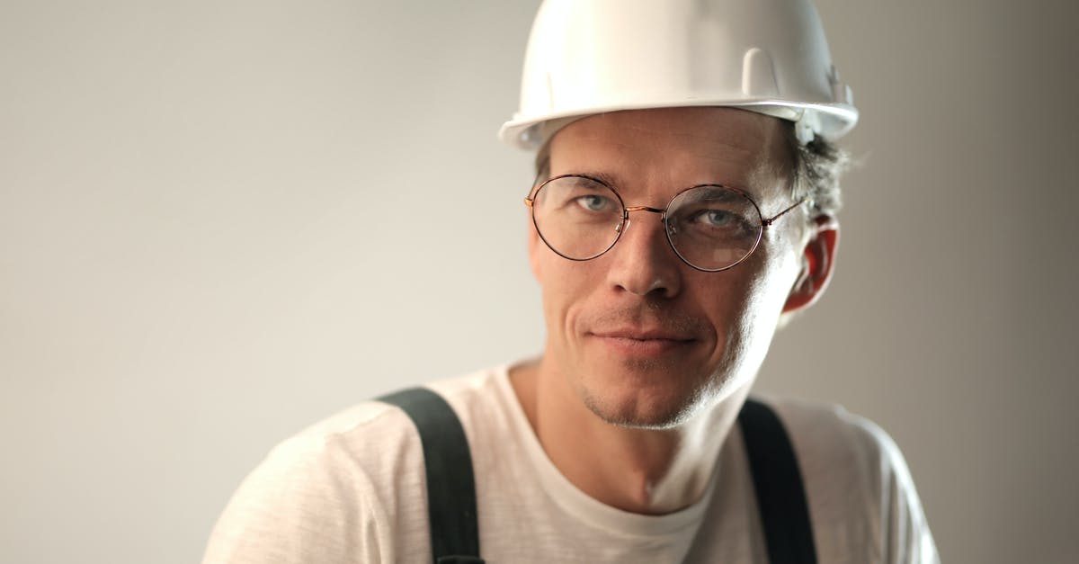 Is it allowed to wear a bulletproof vest in Hong Kong? [closed] - Content male builder in workwear and hardhat smiling on gray background in studio and looking at camera