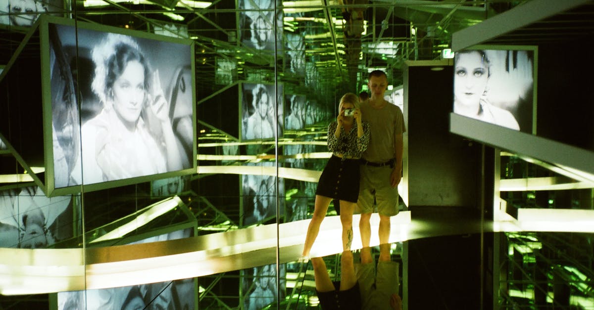Is it legal to take photos at the airport? - Man and Woman Standing Near Photo of Woman Inside Glass Room Is it legal to take photos at the airport? - Man and Woman Standing Near Photo of Woman Inside Glass Room