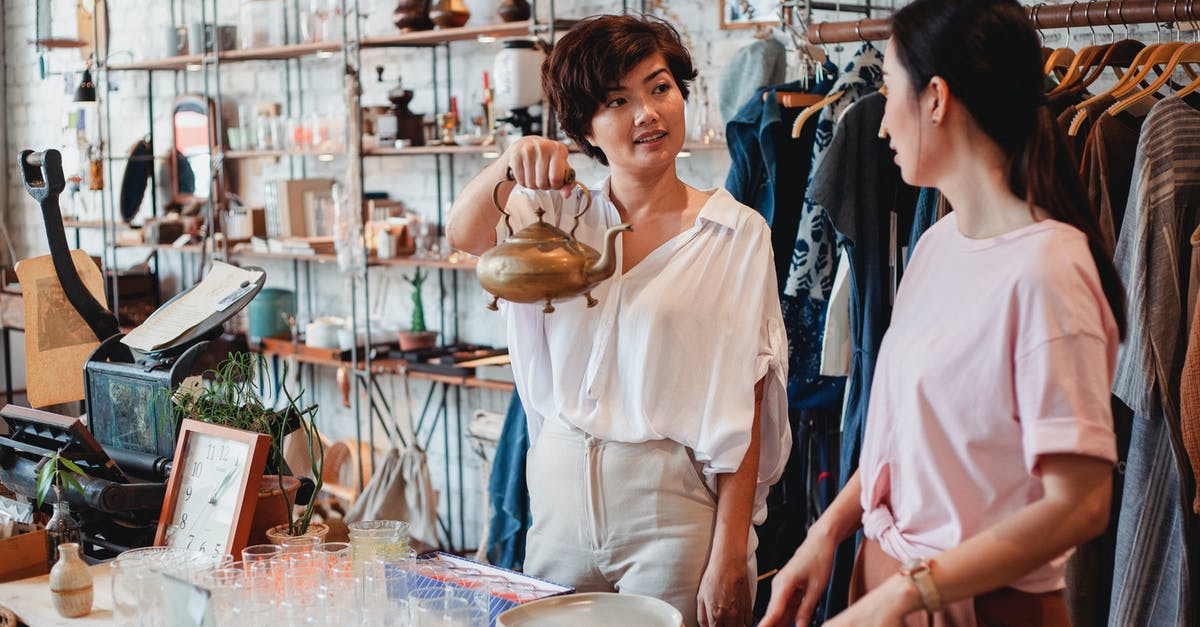 Is it mandatory to show the boarding pass at a duty free shop in the UK? - Young ethnic female shopper demonstrating metal kettle to partner while interacting near table with dishware in store and looking at each other Is it mandatory to show the boarding pass at a duty free shop in the UK? - Young ethnic female shopper demonstrating metal kettle to partner while interacting near table with dishware in store and looking at each other