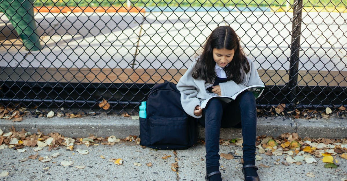 Is it necessary to book a ferry ticket in advance in September for Greece? - Full body concentrated schoolgirl in warm sweater reading topic in textbook while sitting on ground near net fence in autumn park
