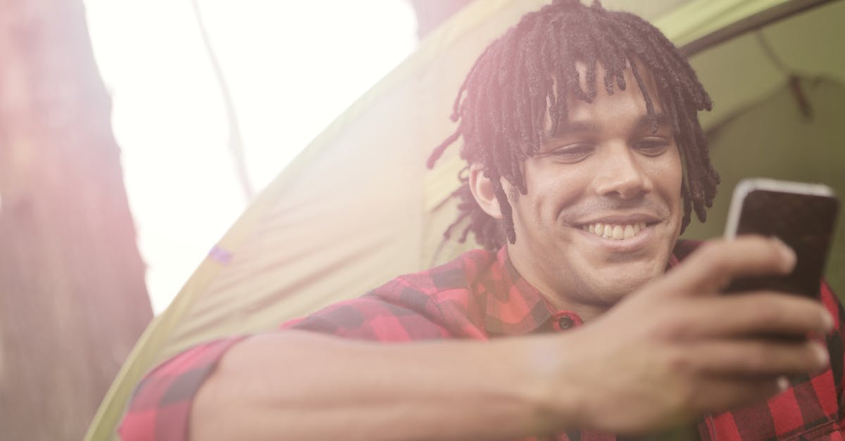 Is it possible to travel around the world using JUST Low-cost carriers? - Young casually dressed man smiling while sitting near tent and surfing smartphone in back lit