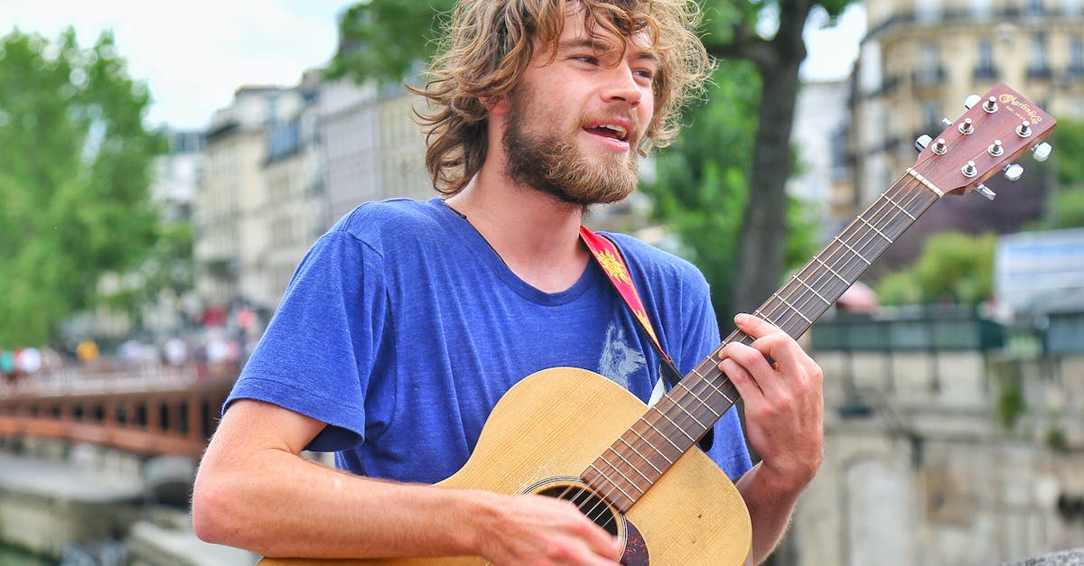 Is it practical to live in Stockholm's inner city while studying in Kista? [closed] - Positive young male musician in casual wear playing acoustic guitar and singing while standing on old city street on sunny summer day