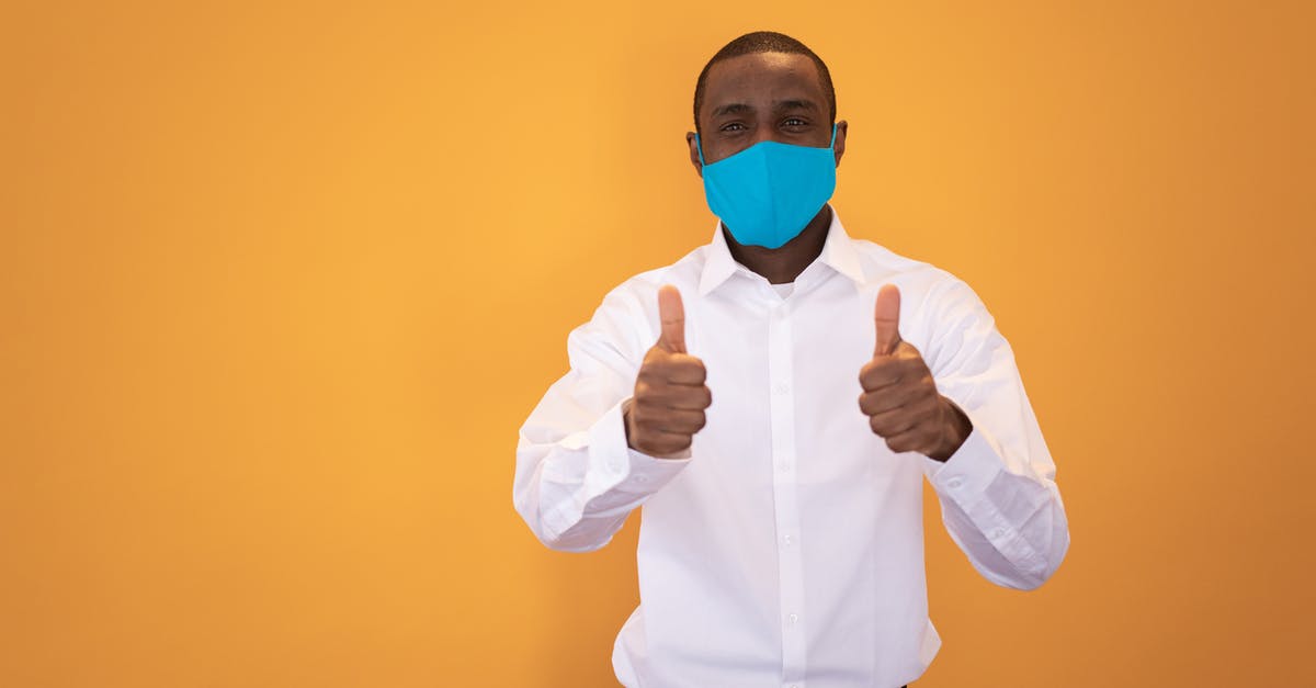 Is it safe to show a biometric passport to a third party? - Positive African American male in protective mask and shirt standing and showing thumbs up gesture against yellow background in studio