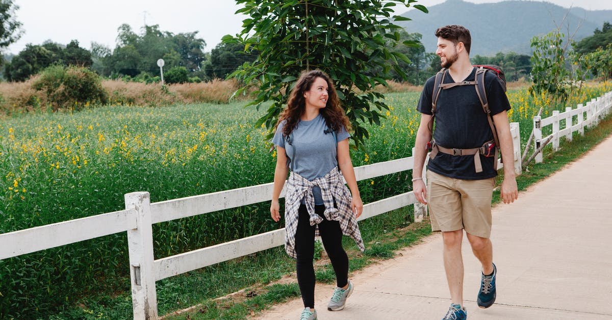 Is there a certain length of time in which you are allowed to travel with the Schengen area? Or Is at each countries discretion? [duplicate] - Full body of young couple of tourists wearing casual clothes and backpacks walking near weathered wooden fence and green grassy meadow with flowers near trees and looking at each other