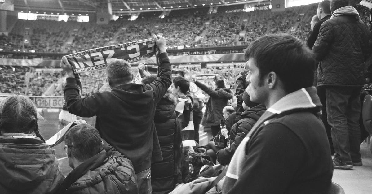 Is there any public place to watch the Olympic games in Singapore? [closed] - Black and white of group of people in warm clothing standing at stadium and watching match