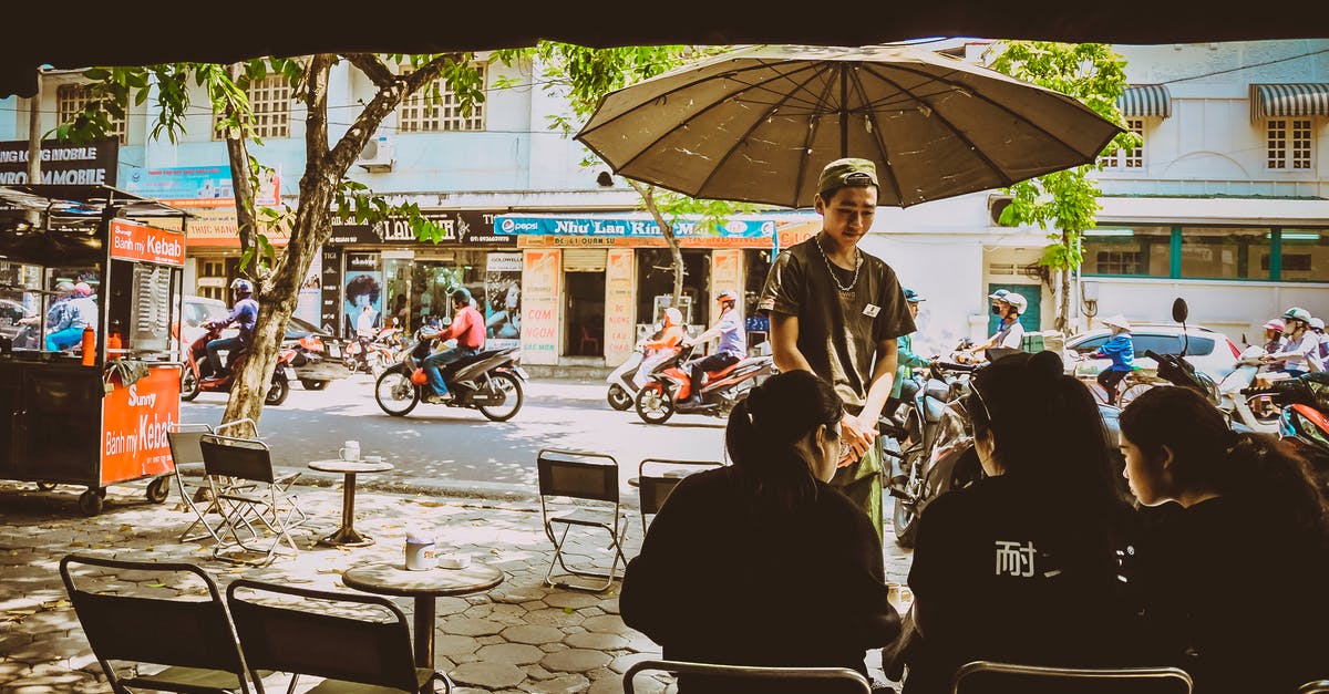 Is there ferry service from Vietnam to Borneo? - Man Standing Beside Umbrella Facing Three Women Sitting On Chairs Is there ferry service from Vietnam to Borneo? - Man Standing Beside Umbrella Facing Three Women Sitting On Chairs