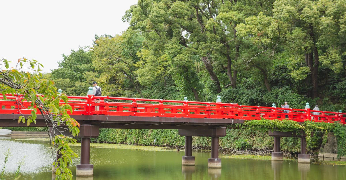 Japan cheapest way to travel? Is carpool/ride share common in Japan? - Tourists walking on red bridge crossing green pond located among lush tropical forest in Japan Japan cheapest way to travel? Is carpool/ride share common in Japan? - Tourists walking on red bridge crossing green pond located among lush tropical forest in Japan