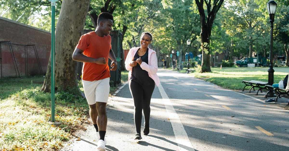 Jogging in Bucharest? - Man in White Tank Top and Black Pants Holding a Phone Walking on the Street during Jogging in Bucharest? - Man in White Tank Top and Black Pants Holding a Phone Walking on the Street during