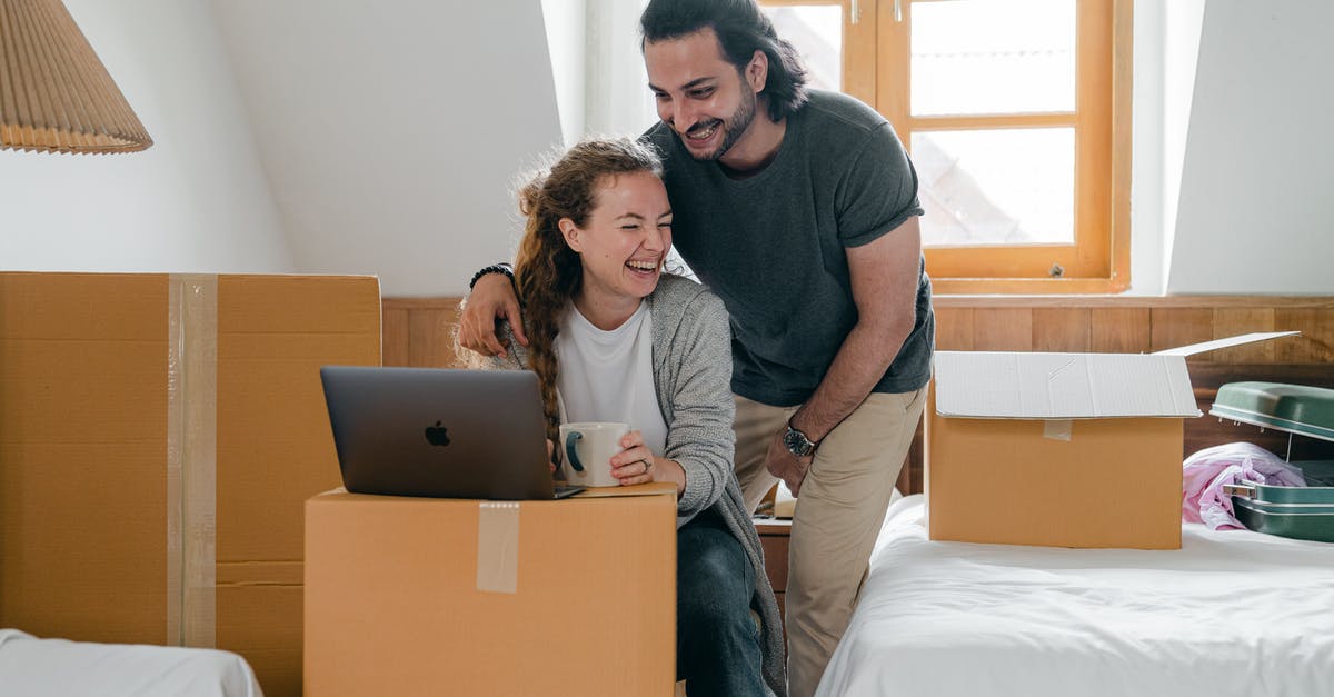 Laptop in a suitcase - Happy diverse couple with laptop sitting in attic style bedroom Laptop in a suitcase - Happy diverse couple with laptop sitting in attic style bedroom