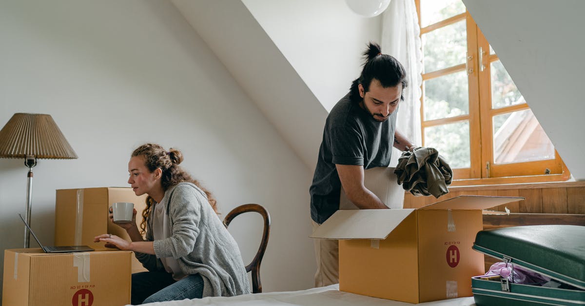 Laptop in a suitcase - Ethnic boyfriend unpacking box while woman using laptop at home Laptop in a suitcase - Ethnic boyfriend unpacking box while woman using laptop at home