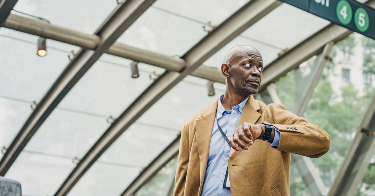 Late Check In rules - Serious African American businessman in formal clothes standing in subway station and checking time on wristwatch while looking away thoughtfully Late Check In rules - Serious African American businessman in formal clothes standing in subway station and checking time on wristwatch while looking away thoughtfully