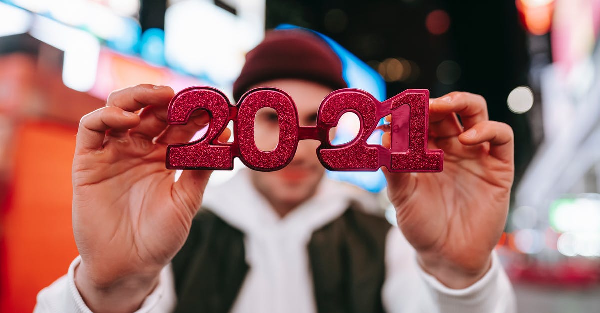 Late no-show at hotel - Anonymous male in hat demonstrating red new years 2021 glasses while standing on street with blurred signboards on modern buildings at night time Late no-show at hotel - Anonymous male in hat demonstrating red new years 2021 glasses while standing on street with blurred signboards on modern buildings at night time