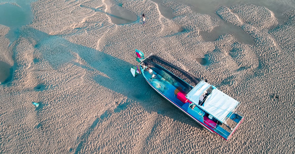 Location in ocean furthest from any land. Are there any established organized travel options for a tourist? - From above of large boat moored on sandy beach with people exploring coast in sunny day Location in ocean furthest from any land. Are there any established organized travel options for a tourist? - From above of large boat moored on sandy beach with people exploring coast in sunny day
