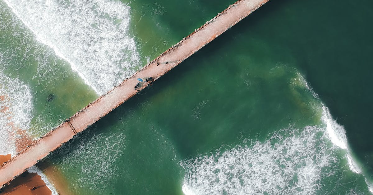 Long term vacation on Falkland islands? - Top view of wavy sea with sandy coast of beach and long concrete bridge Long term vacation on Falkland islands? - Top view of wavy sea with sandy coast of beach and long concrete bridge