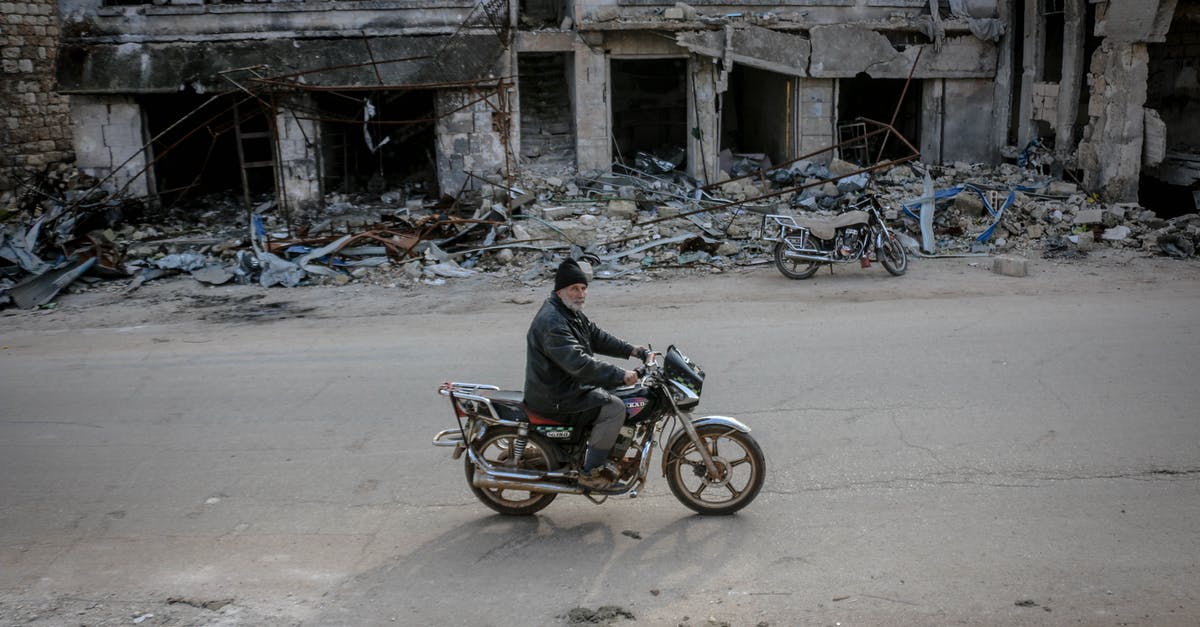 Longest uninhabited road segments - Man riding motorbike along destroyed building Longest uninhabited road segments - Man riding motorbike along destroyed building