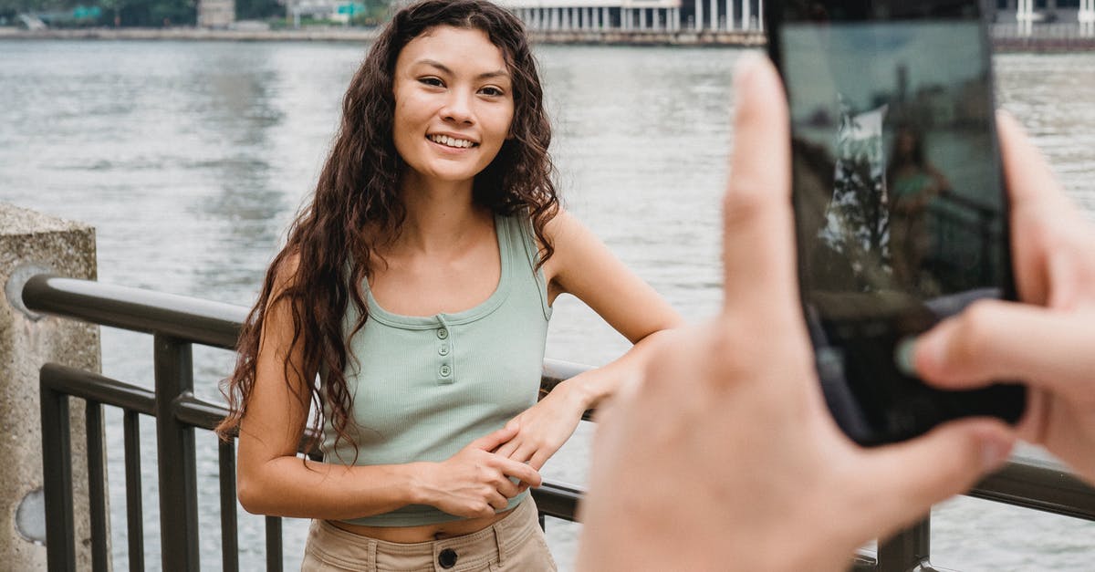 Long-term travel with youth mobility visa? - Unrecognizable person photographing smiling ethnic female friend on smartphone on embankment