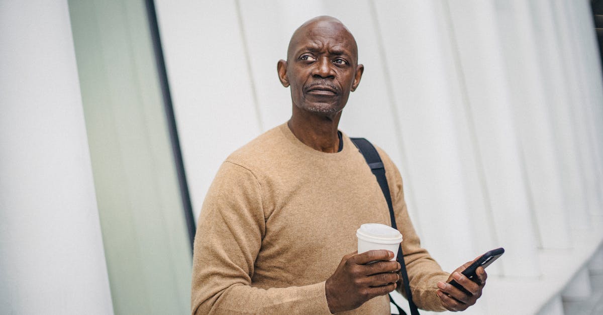 Lost & Found Mobile Telepone - Mature bald black man with smartphone and coffee cup standing on street looking around in downtown Lost & Found Mobile Telepone - Mature bald black man with smartphone and coffee cup standing on street looking around in downtown
