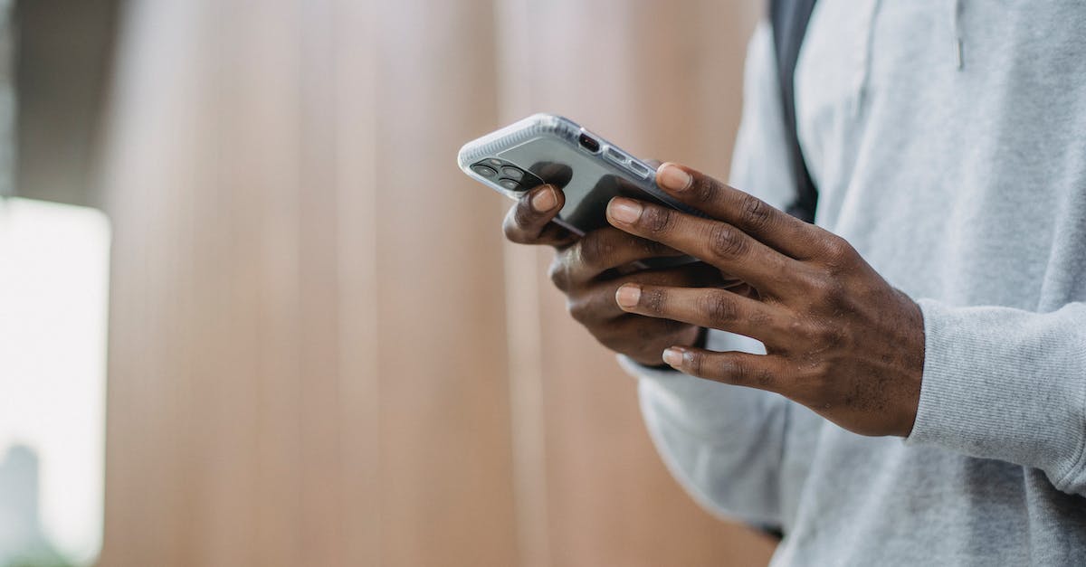 Low cost airlines search engine? - From below crop of unrecognizable African American young guy in casual clothes messaging on mobile phone while standing near wooden wall Low cost airlines search engine? - From below crop of unrecognizable African American young guy in casual clothes messaging on mobile phone while standing near wooden wall