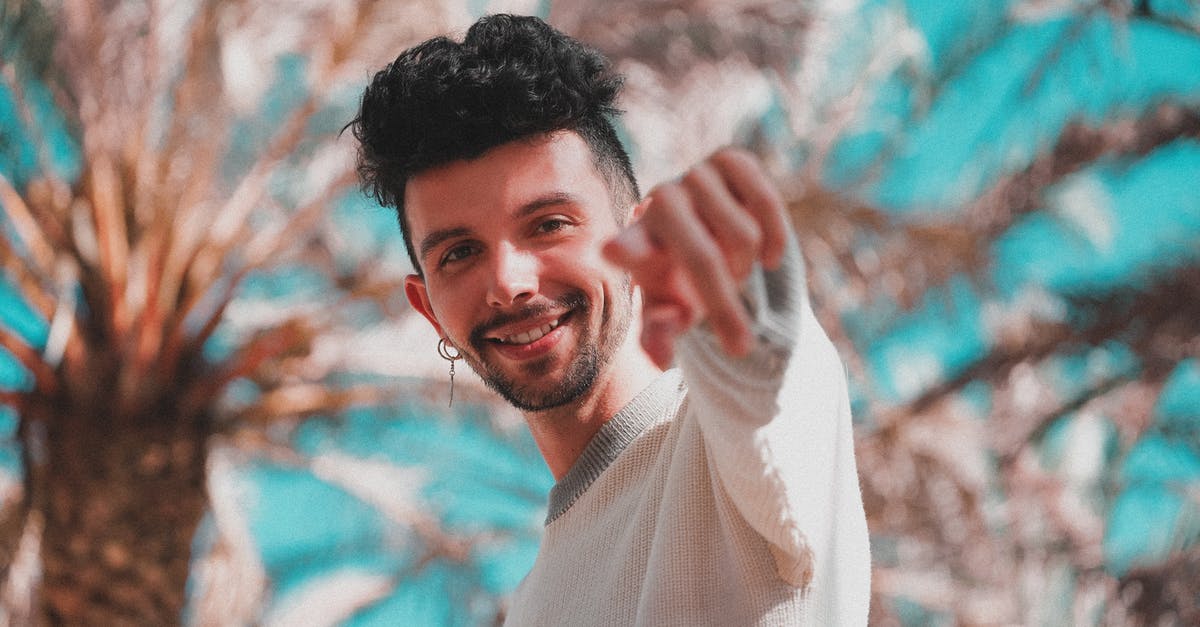 Manual or Automatic transmission: Do rental companies let you choose which type of car you want to rent? - Low angle of modern trendy man with earring pointing with finger at camera standing under palm trees in sunshine