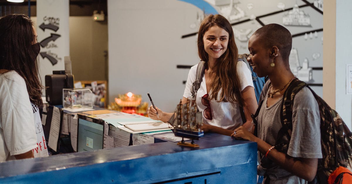 Midnight check-in: Hostel in Paris - Two Women with Backpacks Smiling Beside Blue Desk Midnight check-in: Hostel in Paris - Two Women with Backpacks Smiling Beside Blue Desk
