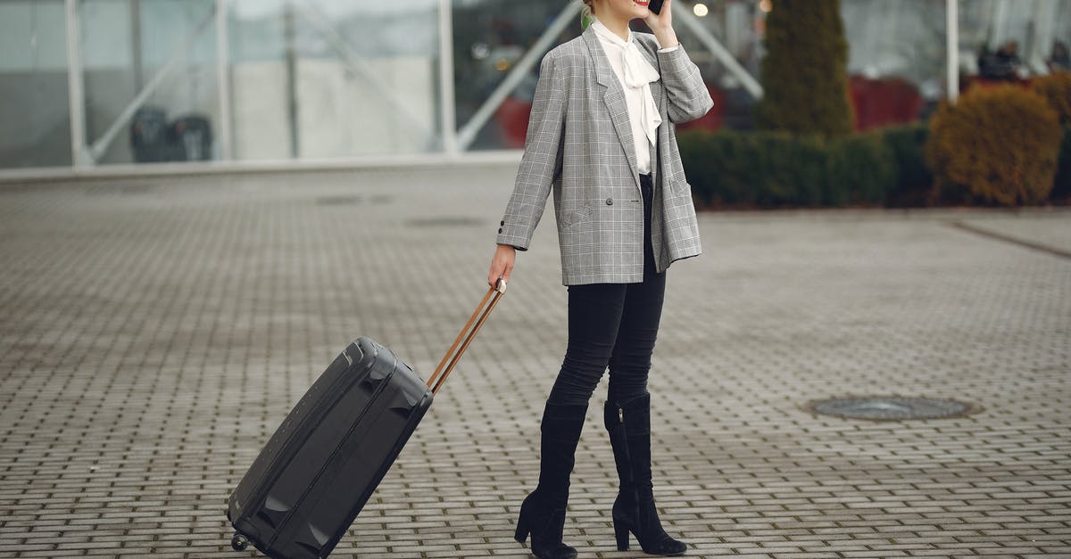 Missed a connection due to delayed baggage - Full body of elegant female tourist in stylish clothes standing with suitcase and calling taxi by phone after arrival in modern city Missed a connection due to delayed baggage - Full body of elegant female tourist in stylish clothes standing with suitcase and calling taxi by phone after arrival in modern city
