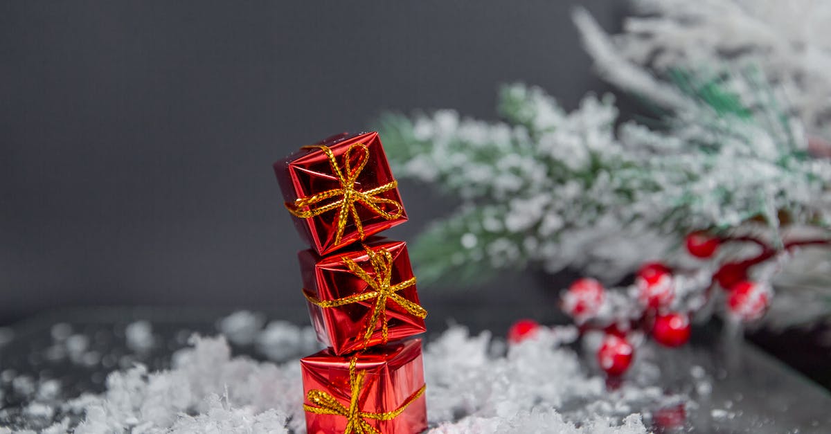 More creative snow festivals than Sapporo snow festival - Small gift boxes wrapped in shiny red paper and tied with golden bows stacked on table covered with snow near Christmas tree against gray wall More creative snow festivals than Sapporo snow festival - Small gift boxes wrapped in shiny red paper and tied with golden bows stacked on table covered with snow near Christmas tree against gray wall