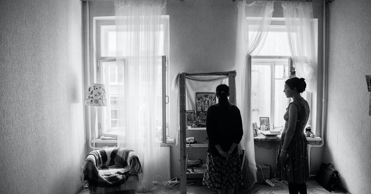 Moving between terminals at Heathrow to visit a lounge - Black and white of anonymous women discussing pictures on shelf in living room with armchair Moving between terminals at Heathrow to visit a lounge - Black and white of anonymous women discussing pictures on shelf in living room with armchair