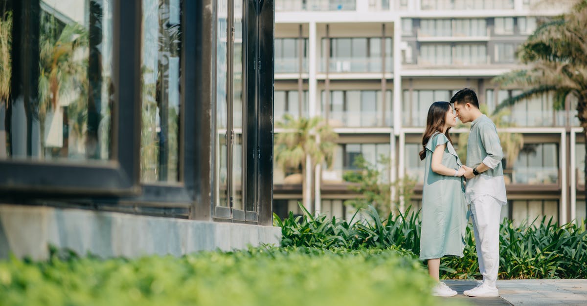 My pregnant wife with Green card status is stuck in India due to COVID-19, What are my options as she cannot come until she gives birth? [closed] - Gentle Asian couple holding hands among modern buildings